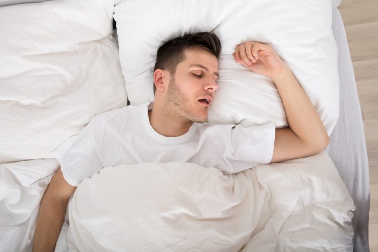 A man snoring while sleeping on a white bed